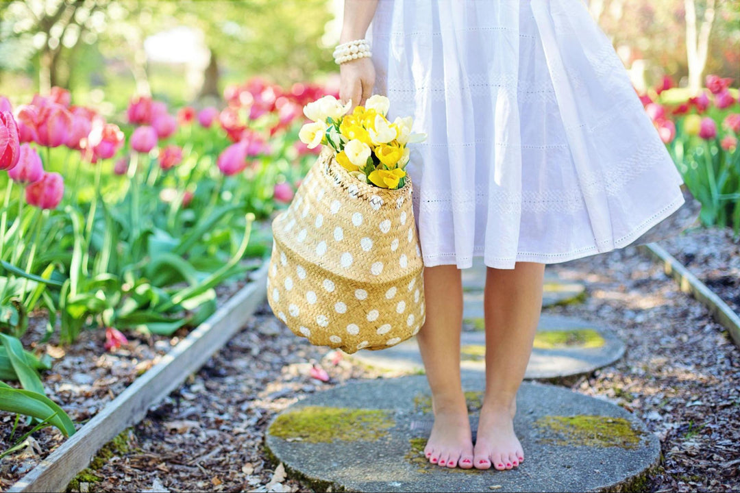 A person standing in a garden surrounded by pink tulips holding a bag of flowers